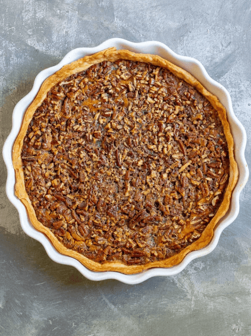 Overhead view of a baked pecan-topped pumpkin pie in a fluted white ceramic dish—an inspiring example of what to do with leftover pumpkin puree for an easy and creative pumpkin pie dessert.