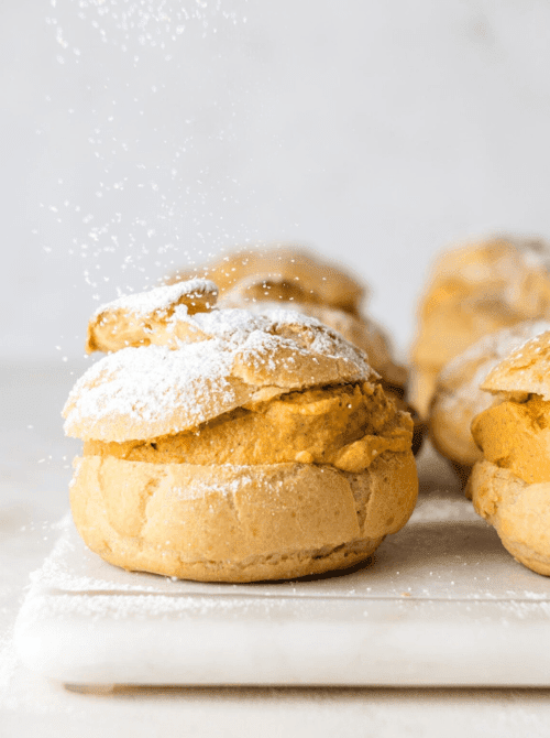 Pumpkin cream puff dusted with powdered sugar, filled with a rich pumpkin purée filling—an elegant and unexpected way to use leftover pumpkin puree for an easy fall dessert.