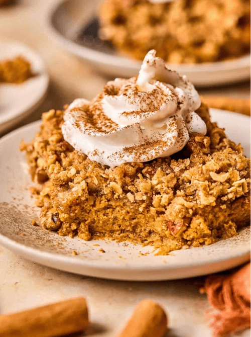 Pumpkin pie crumble bar topped with whipped cream and cinnamon on a beige plate—an easy, comforting way to repurpose leftover pumpkin puree into a cozy fall dessert.