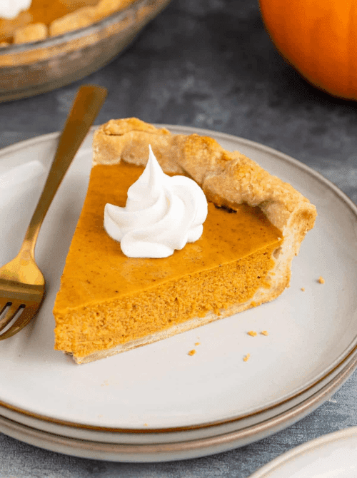 A single slice of pumpkin pie topped with whipped cream, served on a stacked plate with a gold fork—an elegant, easy idea for what to do with leftover pumpkin puree during fall baking season.