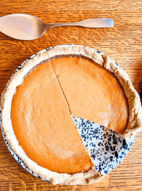 Classic pumpkin pie with a golden crust and one slice removed, displayed on a speckled plate—an easy dessert idea for what to do with leftover pumpkin puree.