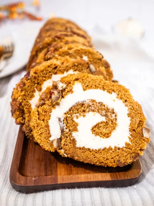 Sliced pumpkin roll filled with cream cheese frosting and topped with chopped pecans—a festive pumpkin dessert and a beautiful way to use up leftover pumpkin puree.