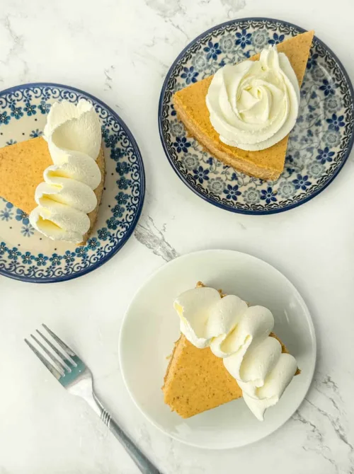 Slices of pumpkin cheesecake topped with piped whipped cream, served on patterned plates — a festive and easy pumpkin cheesecake recipe that’s perfect for fall and a smart way to use up leftover pumpkin purée.