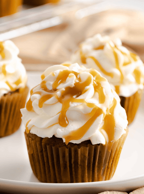 Pumpkin cupcakes topped with fluffy whipped frosting and drizzled with golden caramel sauce—an irresistible example of what to make with leftover pumpkin puree for festive pumpkin cakes and cupcakes.