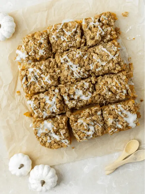 Pumpkin streusel bars with oat crumble topping and a drizzle of icing, cut into squares on parchment paper—an easy fall pumpkin dessert and tasty way to use leftover pumpkin puree.