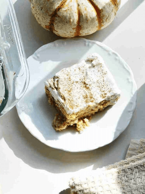 Pumpkin spice cake bar topped with whipped cream and cinnamon, a delicious idea for what to make with leftover pumpkin puree in your next batch of pumpkin cakes and cupcakes.