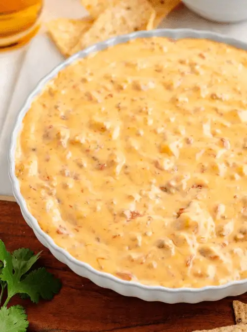 Creamy sausage and cheese dip with diced tomatoes served in a scalloped white dish, perfect for scooping with chips—an easy game day dip that’s always a crowd favorite.