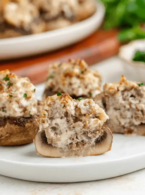 Sausage-stuffed mushrooms with creamy cheese filling, served on a white plate—an easy, elegant bite perfect for football party snacks on a budget.