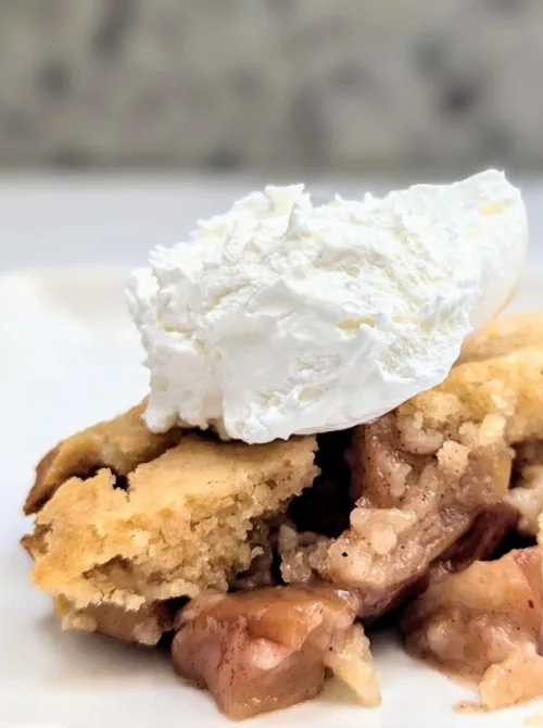 Close-up of warm apple cobbler topped with whipped cream—an easy, comforting fall dessert and one of the most delicious things to make with apples during apple season.