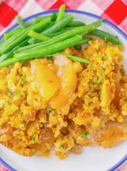 Plate of apple-stuffed chicken casserole with golden cornbread topping, served alongside fresh green beans—a cozy, budget-friendly comfort food perfect for easy fall recipes and satisfying things to make with apples.