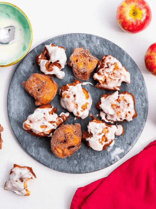 Homemade apple fritters with vanilla glaze on a slate serving platter – simple fall treats made with fresh apples, perfect for cozy autumn baking.