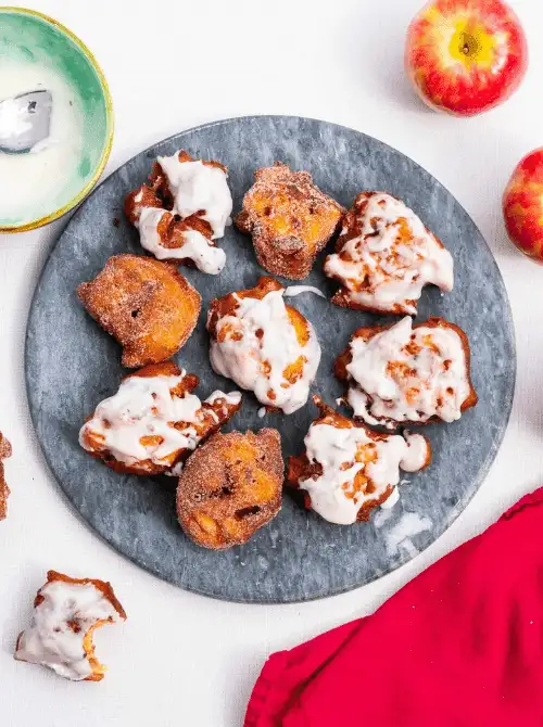 Homemade apple fritters with vanilla glaze on a slate serving platter – simple fall treats made with fresh apples, perfect for cozy autumn baking.