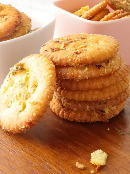 Stack of seasoned Ritz crackers with herbs and spices on a wooden board—crispy, make-ahead tailgate food on a budget that’s easy to serve to a crowd.