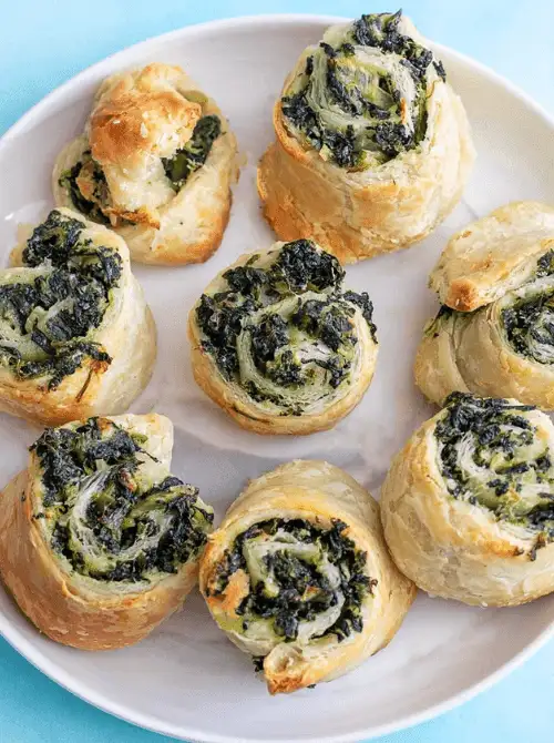 Spinach artichoke pinwheels made with puff pastry, baked to golden perfection and served on a white plate—an easy, crowd-pleasing option for football party snacks on a budget.