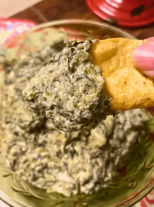 A tortilla chip scooping up creamy spinach dip, perfect for serving as one of your easy game day dips.