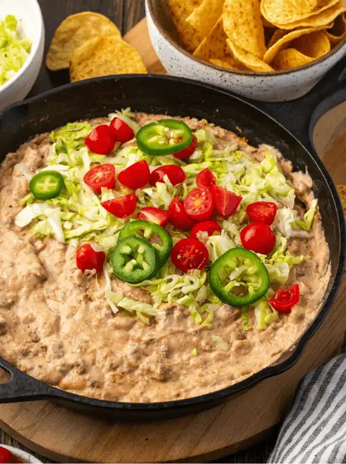 Cast iron skillet filled with creamy taco dip, topped with shredded lettuce, cherry tomatoes, and sliced jalapeños — a bold and flavorful choice for easy game day dips.