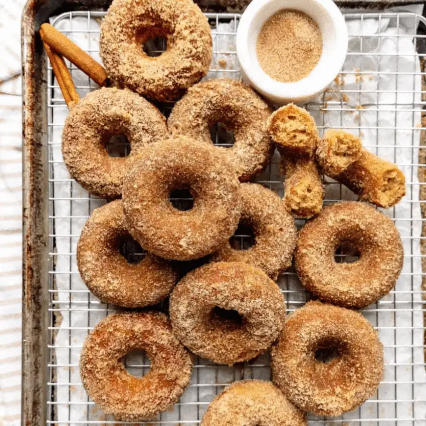 Apple cider donuts coated in cinnamon sugar on a cooling rack with a bowl of spiced sugar—perfect for fall baking and a fun idea for what to make with apples.