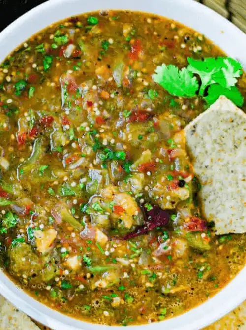A vibrant roasted tomatillo salsa filled with charred peppers, fresh herbs, and diced tomatoes, served in a white bowl with a tortilla chip and fresh cilantro garnish—ideal for football party snacks, easy dips to feed a crowd, and budget-friendly tailgate food.