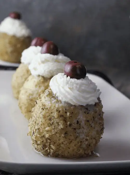 Traditional Hungarian-style dessert dumplings coated in finely ground walnuts, topped with piped whipped cream and a single cherry—an elegant fall treat perfect for festive gatherings.