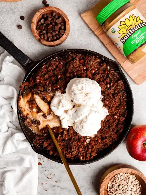 Warm chocolate apple crisp in a cast iron skillet topped with scoops of vanilla ice cream—an indulgent fall dessert and one of the most unexpected yet delicious things to make with apples.