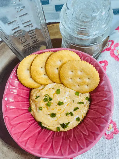 Warm gouda and tahini cream cheese dip served with crackers in a pink bowl—an easy and elegant addition to football party snacks on a budget.