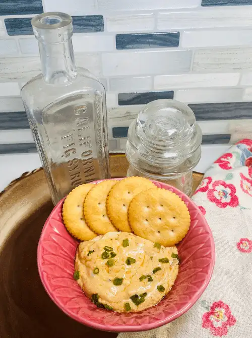 Bowl of creamy dip garnished with chopped green onions, served with round buttery crackers on a wooden tray — a delicious option for easy game day dips.
