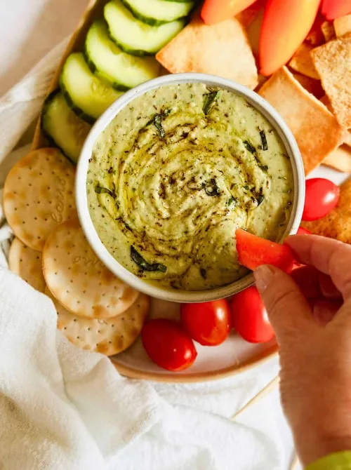 Bowl of herbed green dip surrounded by crackers, cucumbers, tomatoes, and pita chips—an easy game day dip that’s both fresh and flavorful.