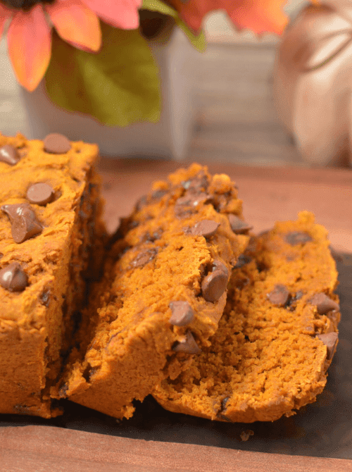 Freshly sliced chocolate chip pumpkin bread on a wooden board with flowers in the background — a delicious idea for what to do with leftover pumpkin puree and a tasty option for easy pumpkin bread recipes.