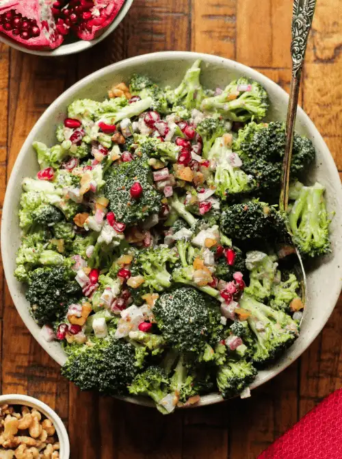 Broccoli salad with creamy dressing, red onion, pomegranate seeds, and walnuts in a ceramic bowl—perfect for Budget-Friendly Thanksgiving Vegetable Sides.