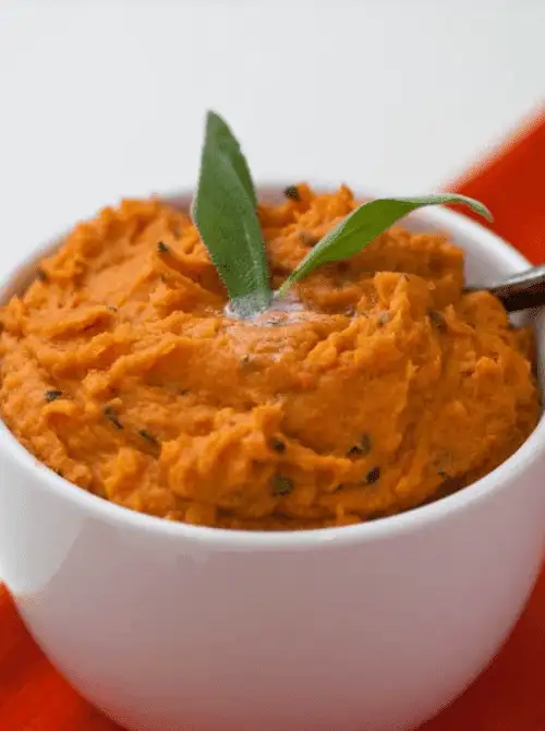 Bowl of browned butter mashed sweet potatoes garnished with fresh sage, featured in Budget-Friendly Thanksgiving Sides and Easy Potato Recipes for a flavorful holiday dish.