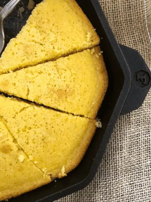 Cast iron skillet with golden baked sweet corn bread sliced into wedges, a classic budget-friendly Thanksgiving side.