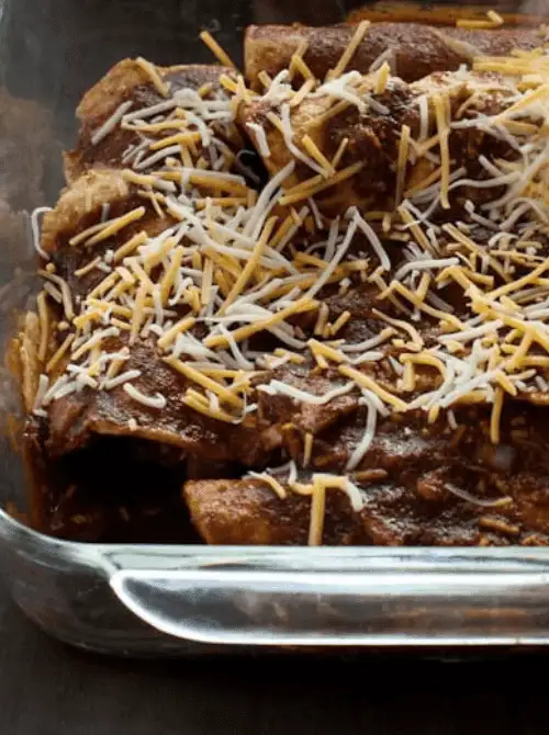 Baking dish of cheesy turkey enchiladas topped with red sauce and shredded cheese — a flavorful twist on what to make with Thanksgiving leftovers and one of the best easy turkey recipes for family dinners.