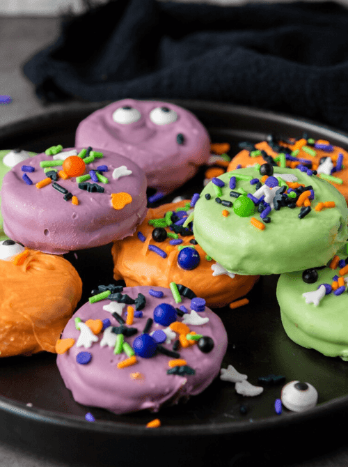 No-Bake Halloween Treats featuring colorful monster-themed Oreo cookies dipped in purple, green, and orange candy melts, topped with festive sprinkles and candy eyes for a playful party-ready dessert.