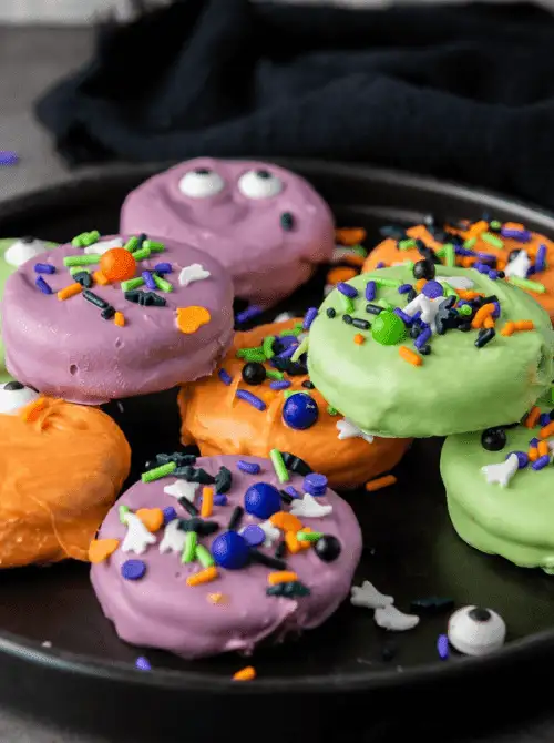 No-Bake Halloween Treats featuring colorful monster-themed Oreo cookies dipped in purple, green, and orange candy melts, topped with festive sprinkles and candy eyes for a playful party-ready dessert.