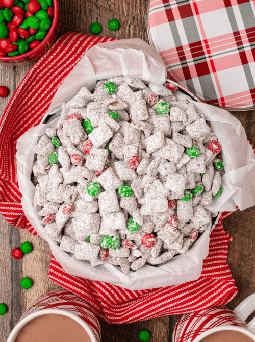 Bowl of Christmas puppy chow coated in powdered sugar with red and green candies, a festive DIY Christmas gift and easy edible gift idea for holiday sharing.