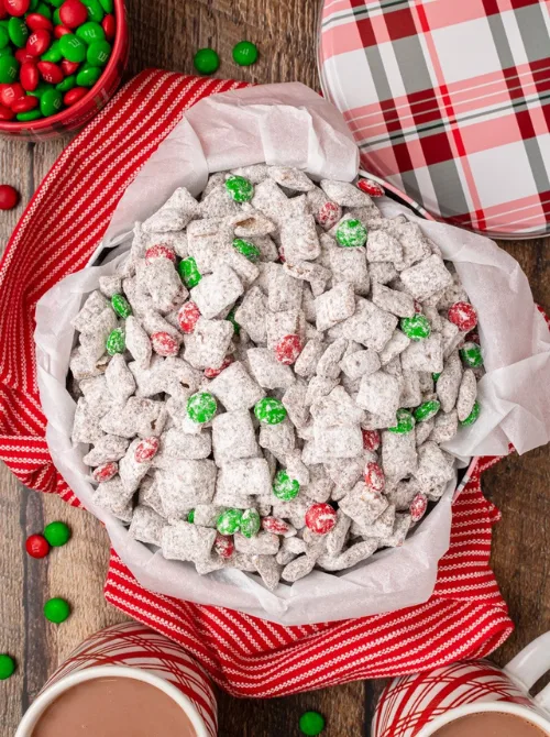 Bowl of Christmas puppy chow coated in powdered sugar with red and green candies, a festive DIY Christmas gift and easy edible gift idea for holiday sharing.