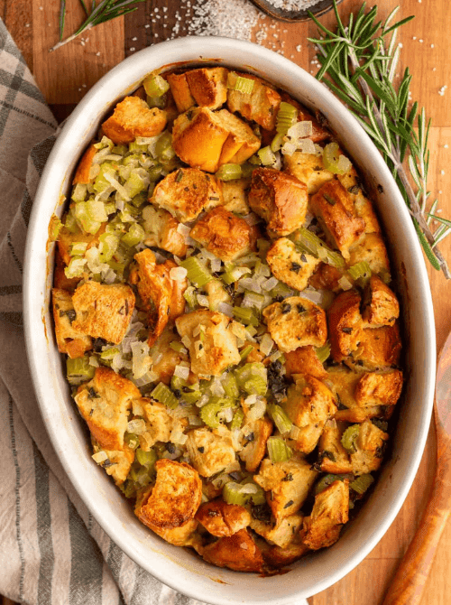 Oval baking dish filled with golden brown bread stuffing with celery and onions, a classic budget-friendly Thanksgiving side dish.