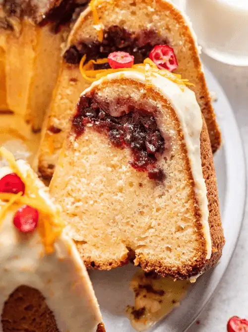 A slice of cranberry-filled bundt cake topped with icing and orange zest – a delicious idea for what to make with Thanksgiving leftovers, perfect for recipes that stretch your budget.