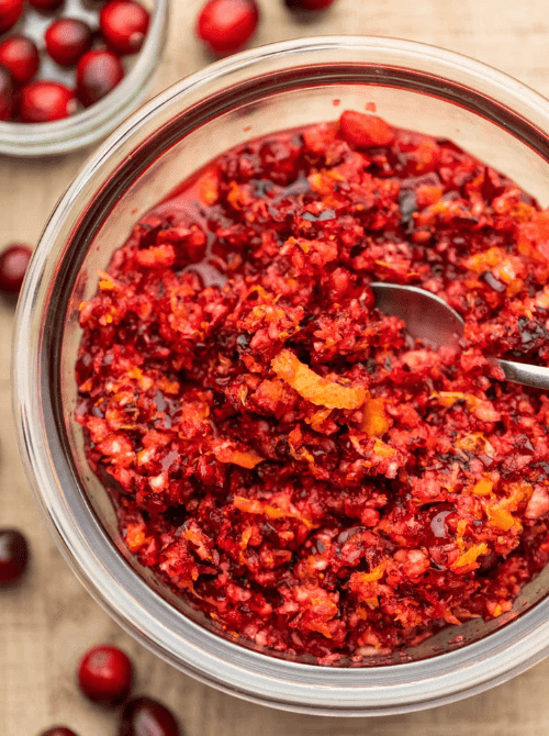 Fresh cranberry orange relish in a glass bowl, a vibrant and budget-friendly Thanksgiving side dish garnished with orange zest.