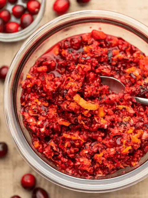 Fresh cranberry orange relish in a glass bowl, a vibrant and budget-friendly Thanksgiving side dish garnished with orange zest.