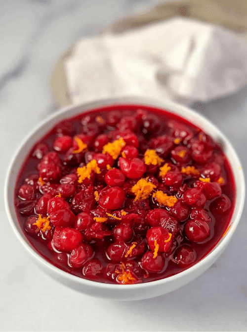 Bowl of homemade cranberry sauce topped with fresh orange zest, a colorful and budget-friendly Thanksgiving side dish.