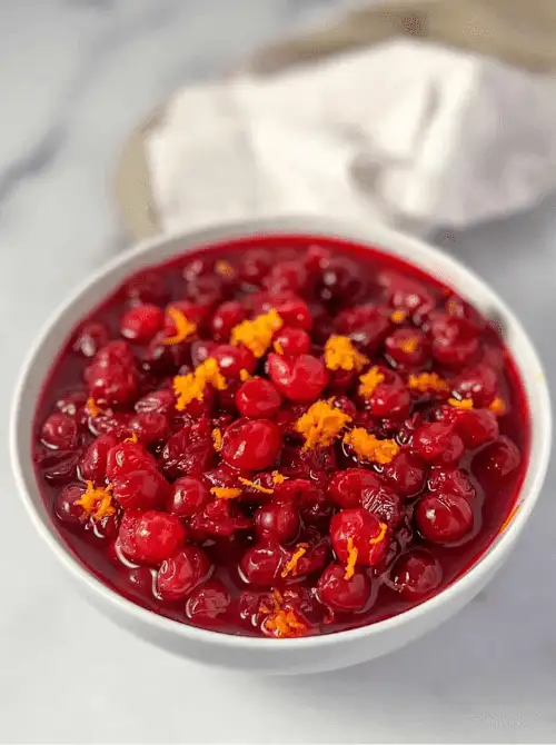 Bowl of homemade cranberry sauce topped with fresh orange zest, a colorful and budget-friendly Thanksgiving side dish.