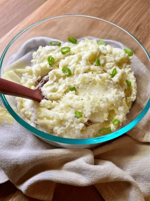 Glass bowl of creamy mashed potatoes topped with sliced green onions, featured in Budget-Friendly Thanksgiving Sides and Easy Potato Recipes for a simple, flavorful holiday dish.