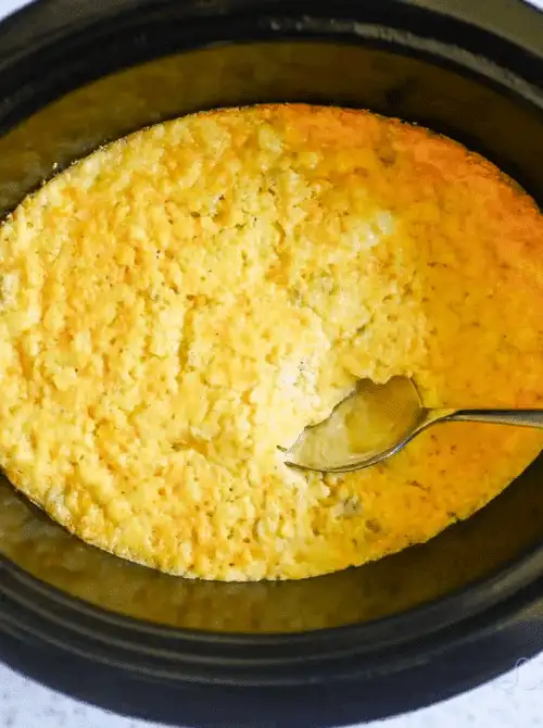 Slow cooker filled with golden baked corn casserole, an easy and budget-friendly Thanksgiving side dish.