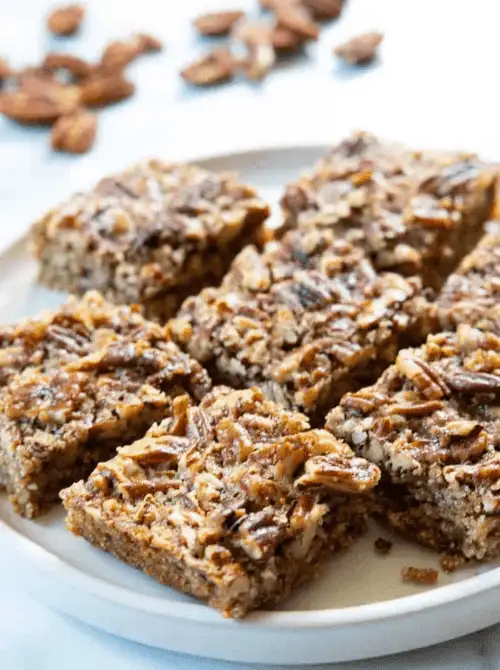Homemade pecan bars on a white plate, a rich and nutty DIY Christmas gift idea featuring cookies and bars.