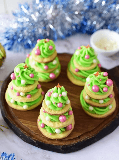 Stacked sugar cookies decorated with green frosting and candy ornaments to look like Christmas trees, a festive DIY Christmas gift idea featuring cookies and bars.