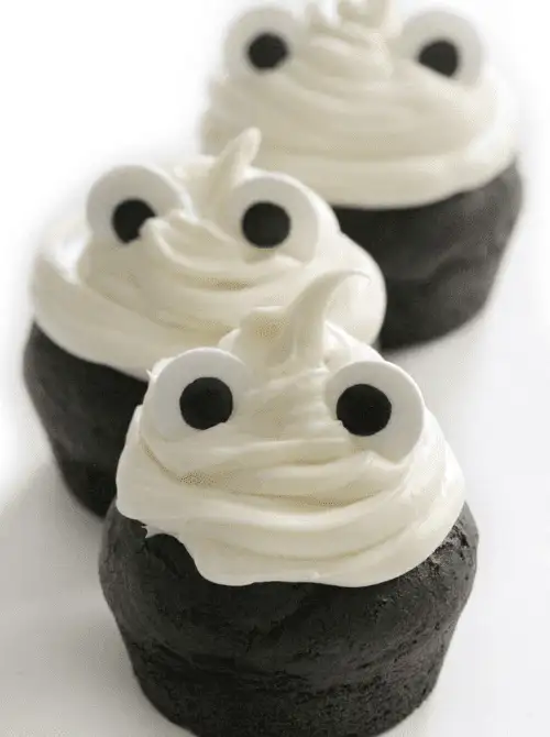 Dark chocolate ghost cupcakes topped with swirled white frosting and candy eyes—easy, allergy-friendly make-ahead Halloween party food that’s spooky and kid-approved.