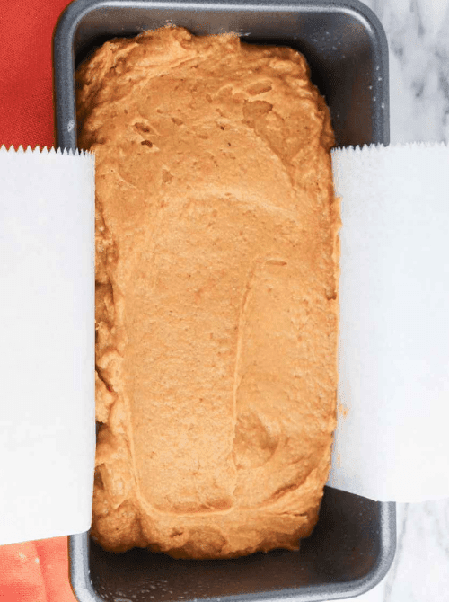 Unbaked pumpkin bread batter in a parchment-lined loaf pan, ready to go into the oven, with a smooth, creamy surface.