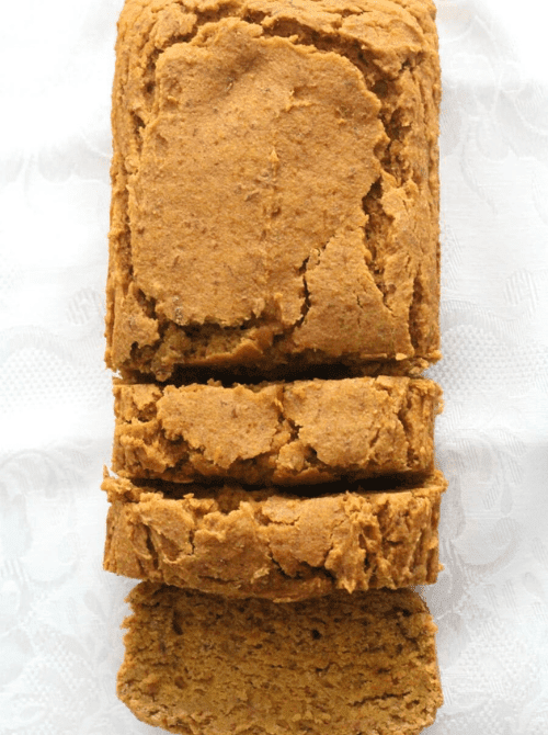 Moist loaf of pumpkin bread with a rustic, crackled top, sliced to reveal its soft, dense interior on a white textured background.