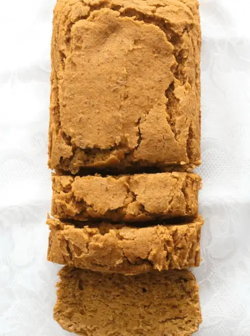 Moist loaf of pumpkin bread with a rustic, crackled top, sliced to reveal its soft, dense interior on a white textured background.